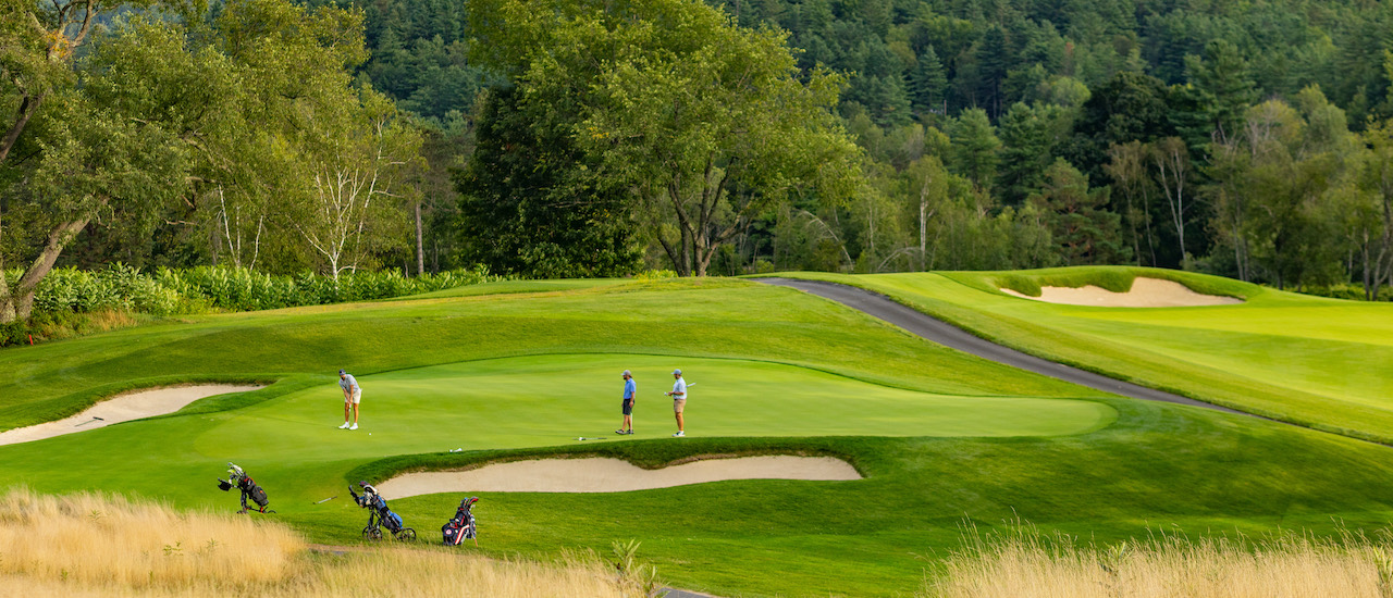 Golfers on a manicured green at Stowe Country Club with the wooded Green Mountains rising behind, Stowe, Vermont